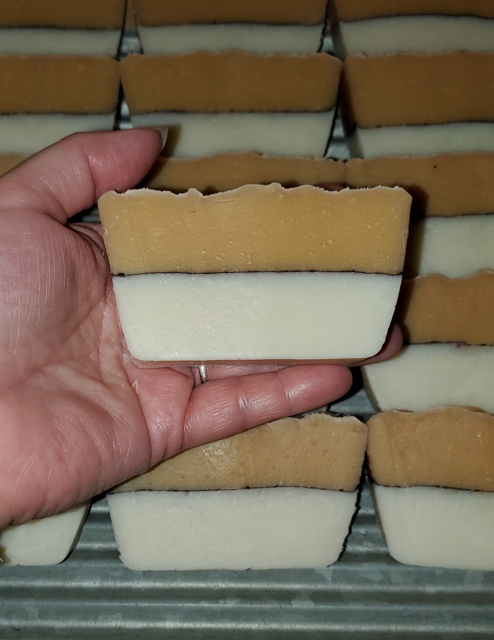 Butterific shea and honey two tone soap shown in a woman's hand with several bars on a washing board in the background.