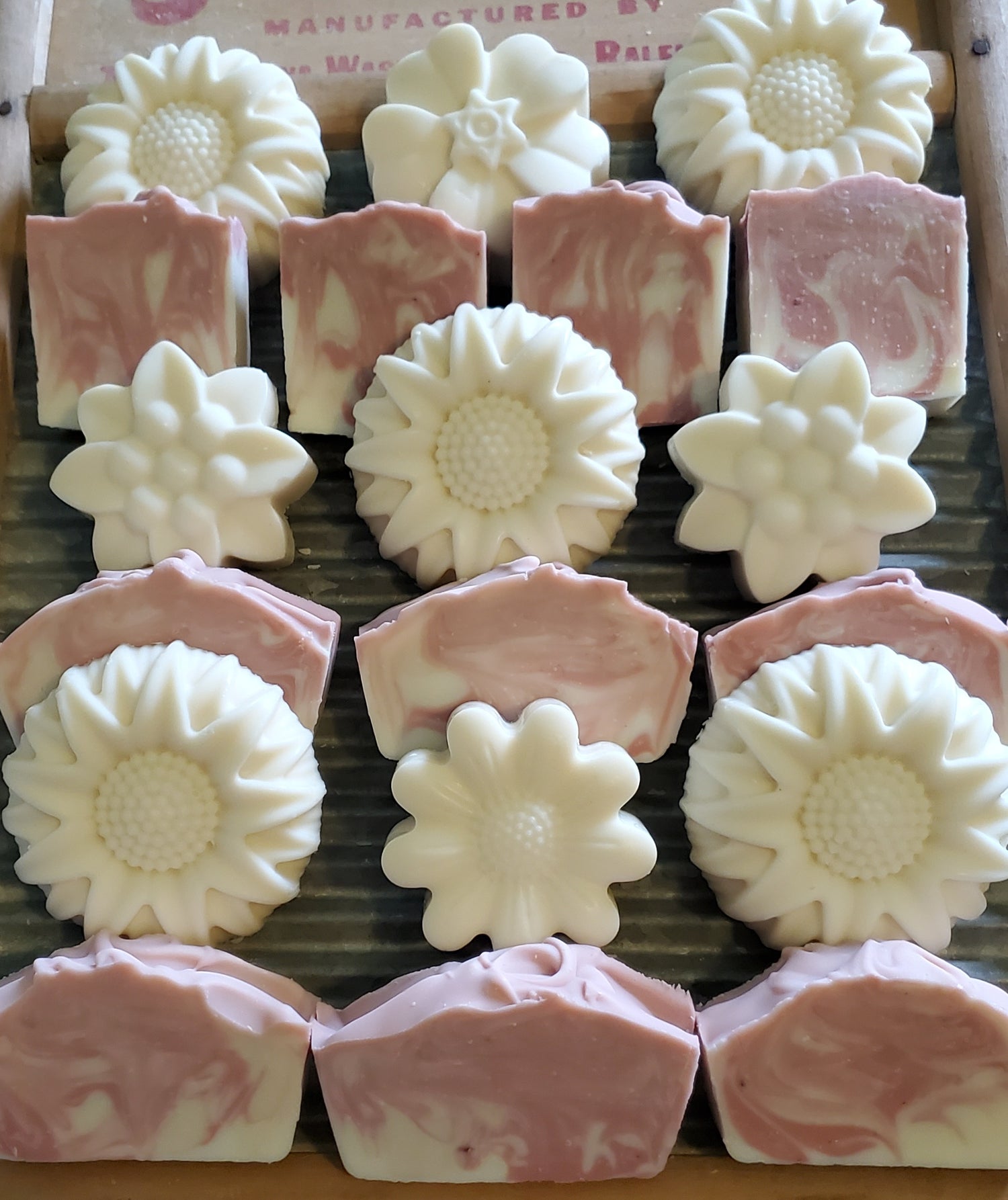 Just Plain Soap pink edition shown (tall and narrow bar in the back,  short and wide bar in the front) displayed with Just Plain floral edition on a washing board. 