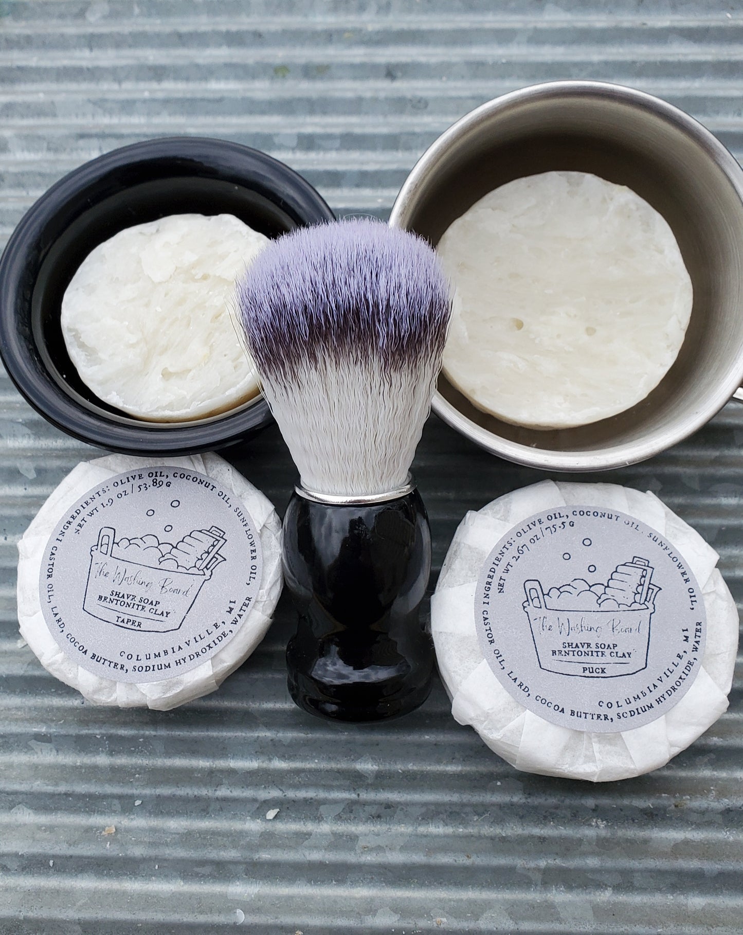Bentonite Clay Shave Soaps, "Naked" Taper in the black bowl, "naked" Puck in the stainless steel cup, a Shave Brush, a wrapped taper and a wrapped puck.