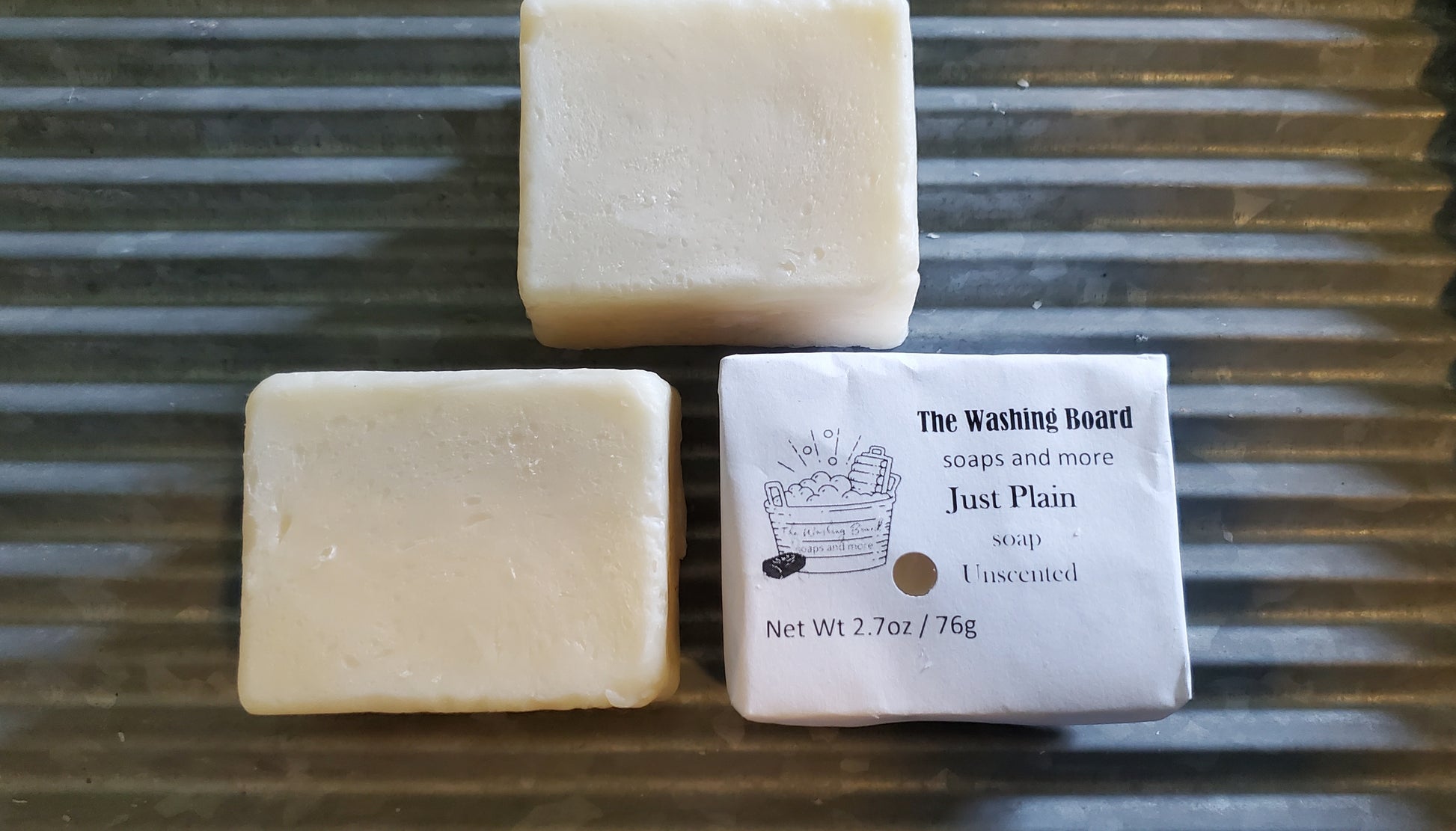 Just Plain Soap bar shown "naked" and in eco friendly packaging on a washing board. 