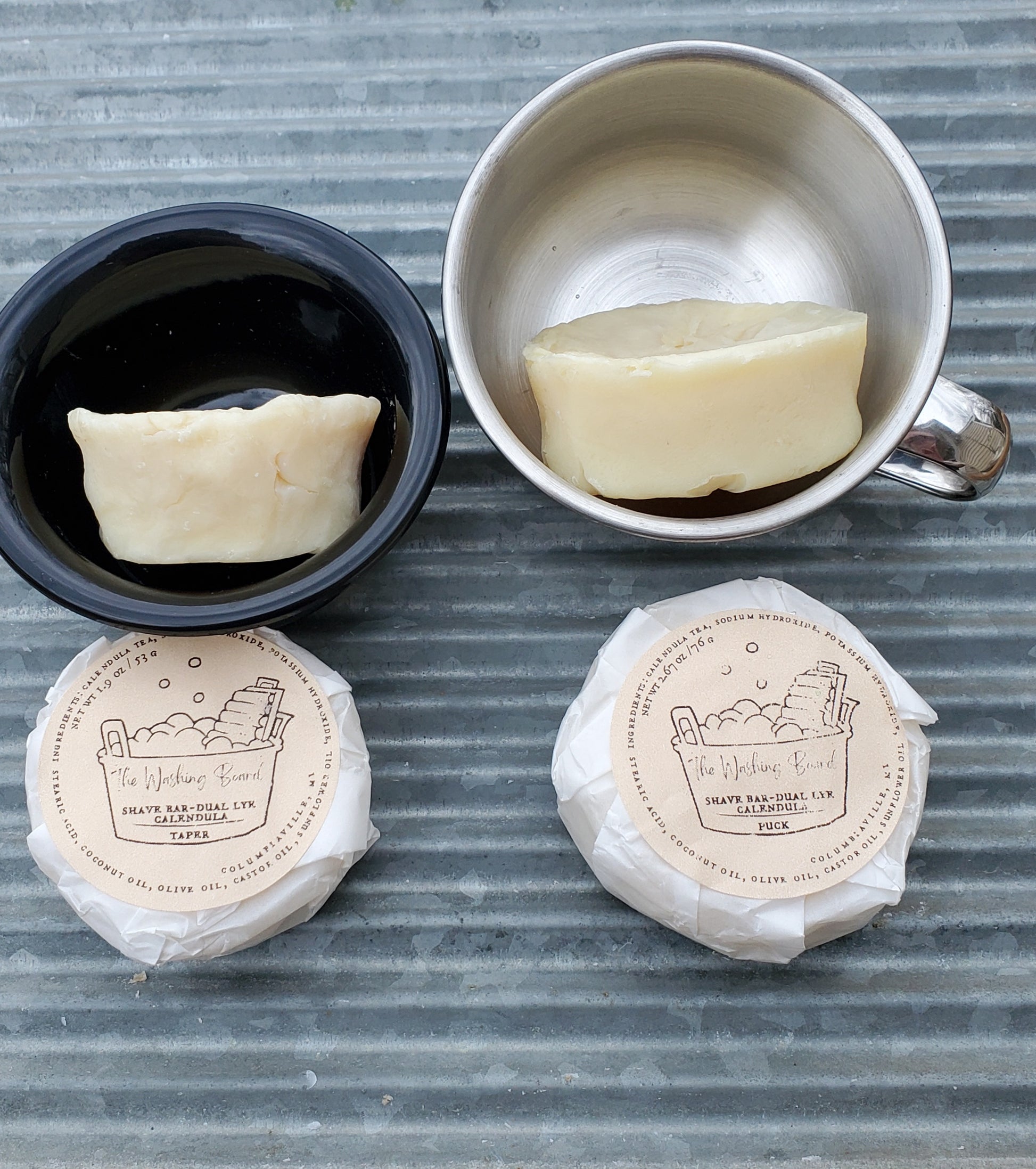 Dual Lye Shave Soaps,  "Naked" Taper on its side in the black bowl, "naked" Puck on its side in the stainless steel cup,  a Shave Brush, a wrapped taper and a wrapped puck.